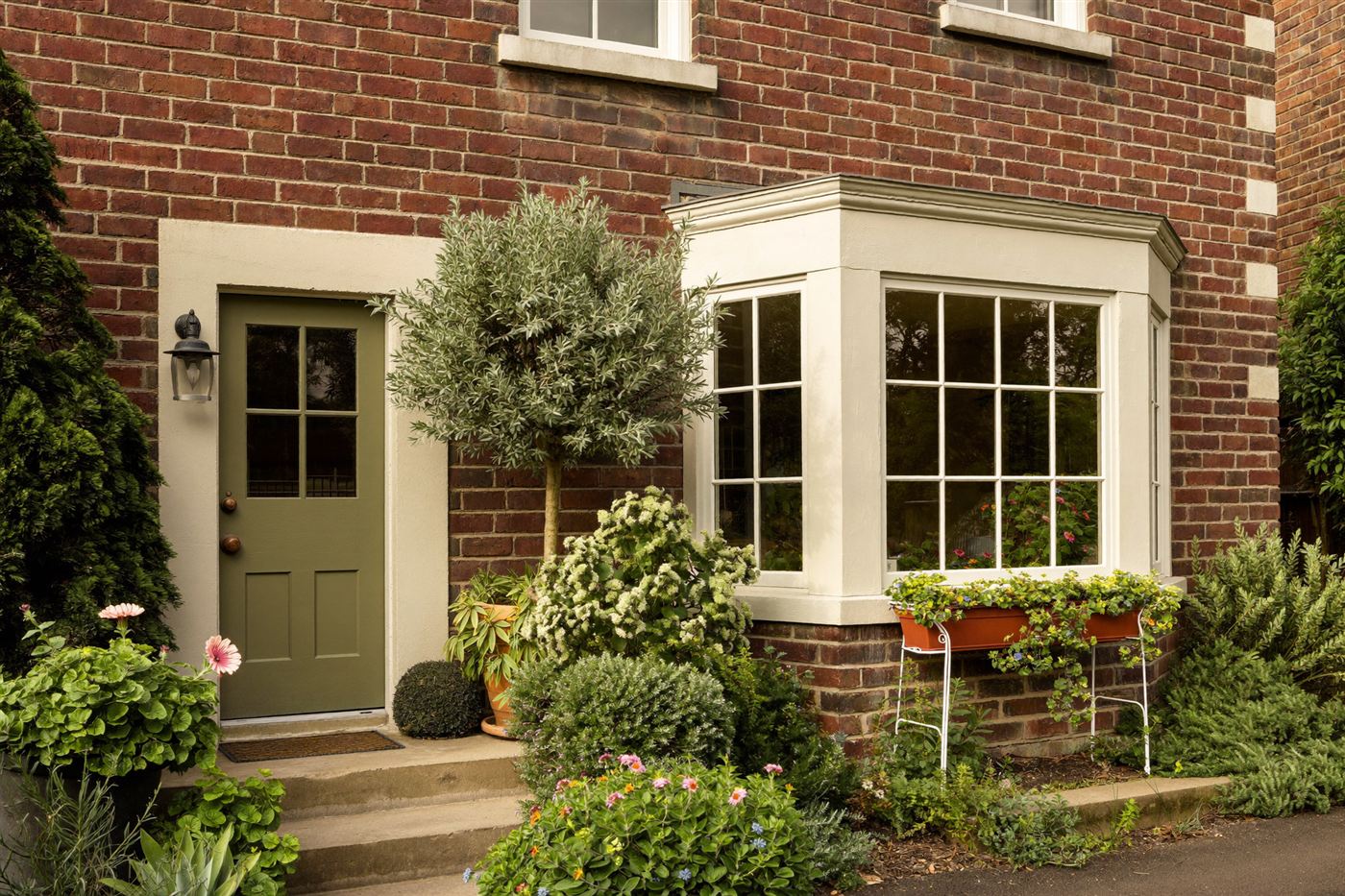 A red-brick house with a sage green front door and potted plants