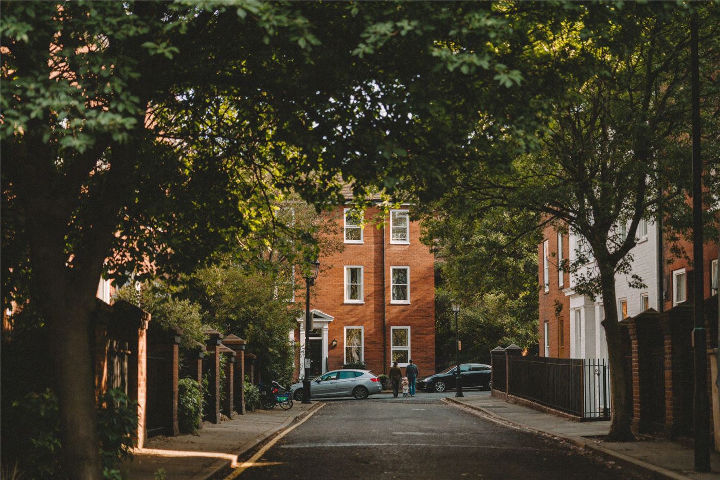 A tree-lined residential street with a family walking in dappled light